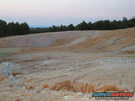 open quarry with dirt mounds and trees in background