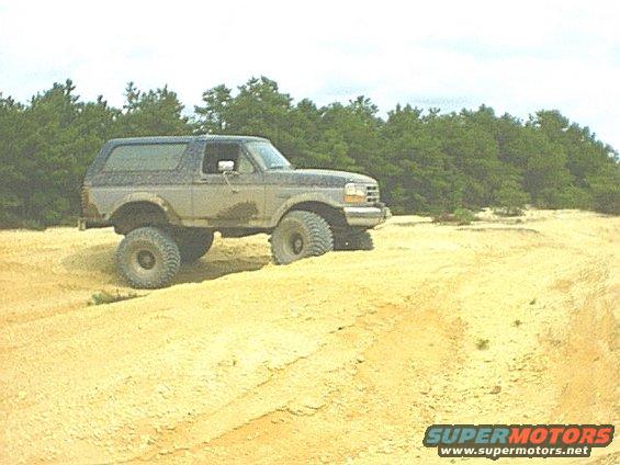 1995 Ford Bronco with lifted suspension driving on a sandy track with trees in the background