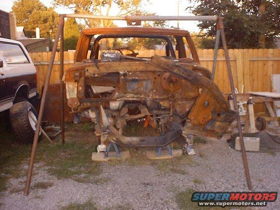 rusted vehicle chassis on stands, another vehicle partially visible to the left