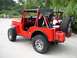 1967 Ford Bronco - A red jeep is parked outdoors with a wooded area in the background and another vehicle behind it.