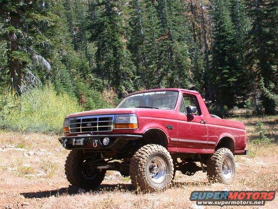 1996 Ford Bronco with lifted suspension and off-road tires parked on a dirt trail with trees in the background