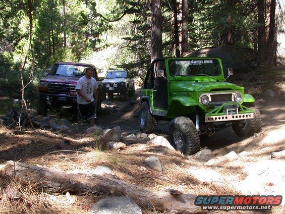 Green off-road vehicle with "Supreme 4 Wheel Drive" text on windshield, and a red truck on a rocky trail