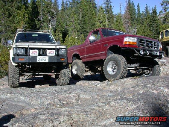 1996 Ford Bronco and a white off-road truck parked on rocks