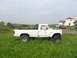 1985 Ford Bronco - Modified white pickup truck sits in a grassy field with a 'A VENDRE' sign in the window.