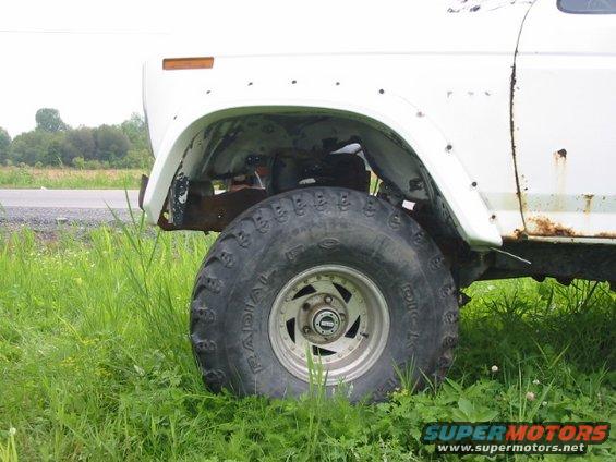 White SUV with large off-road tires and visible rust on the side panel