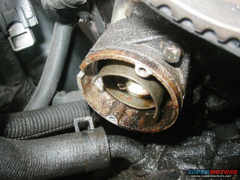 Close-up of a rusty engine component with hoses and a timing belt