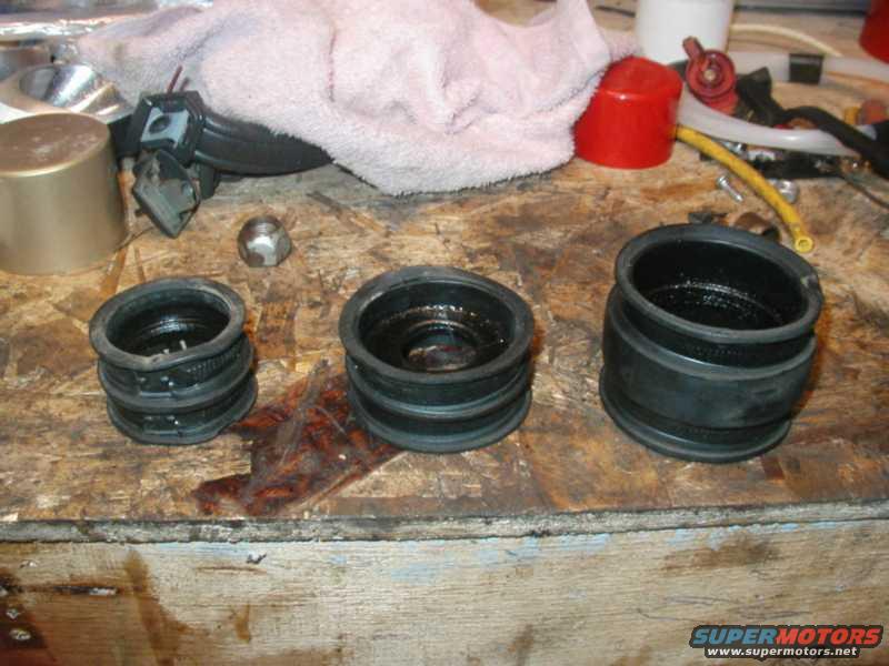 Three rubber intake boots of varying sizes and a metal nut on a wooden surface