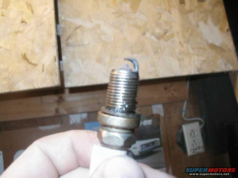 Spark plug held in hand, with metal and ceramic components visible