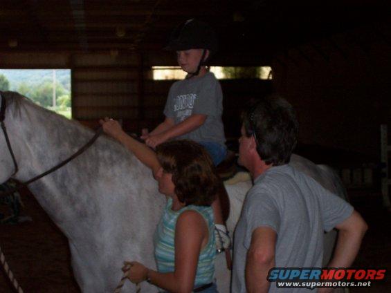 Kid on a horse, with a woman holding the reins and a man standing nearby, inside a barn