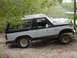 1982 Ford Bronco - A two-tone Ford Bronco sits off-road, partially obscured by trees, with a body style consistent with the early 1980s.