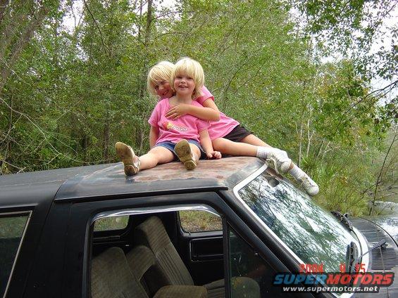 two girls sitting on the roof of a black vehicle, one hugging the other