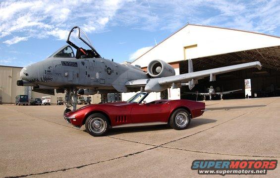 Red 1968 Chevrolet Corvette convertible parked next to an A-10 Thunderbolt II aircraft