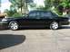 1996 Ford Crown Victoria - A black sedan is parked on a paved surface with trees and houses visible in the background.