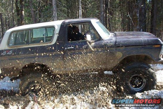 1978 Ford Bronco driving through mud and snow, kicking up spray