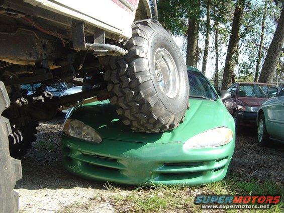 Big tire on green car's hood, other cars in background