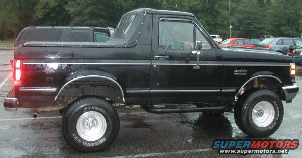 Black Ford Bronco with a soft top, side view, showing chrome trim and aftermarket wheels