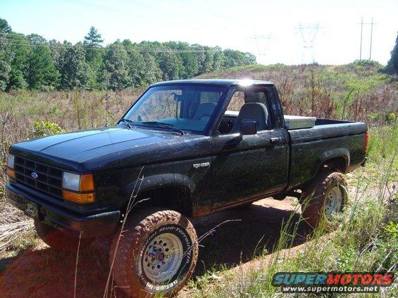 Black Ford Ranger pickup truck on a dirt path with trees and power lines in the background