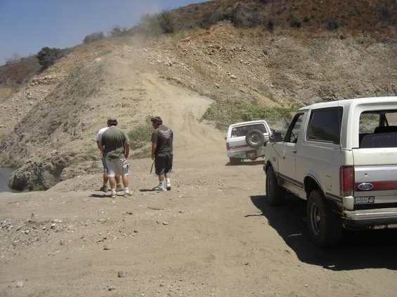 1990 Ford Bronco parked on a dirt road with two other Broncos in the background
