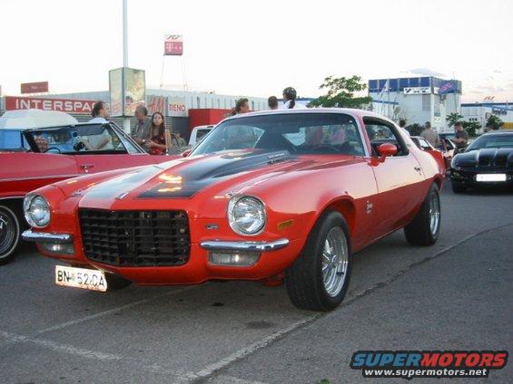 Red 1970s Chevrolet Camaro with black stripes on hood, parked outside