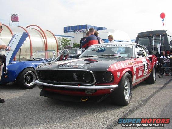 Red and black race car with sponsor decals, parked next to a blue convertible