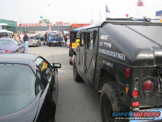 Black Humvee parked next to a black sports car. Text on Humvee reads 'SERVICE, BEZ. TUNING, SONDERANFERTIGUNGEN, WWW.HPP.AT'