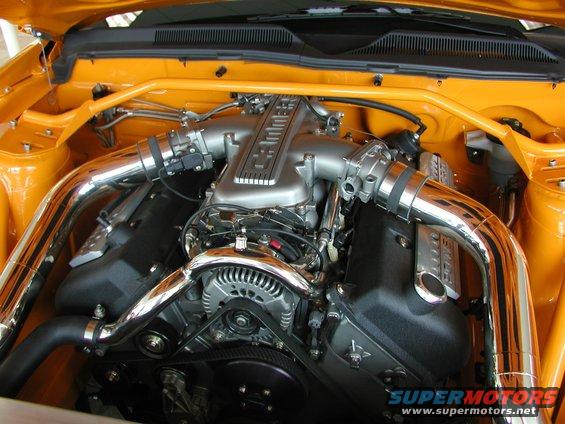 Orange engine bay with a V8 engine, chrome intake pipes, and a yellow strut bar