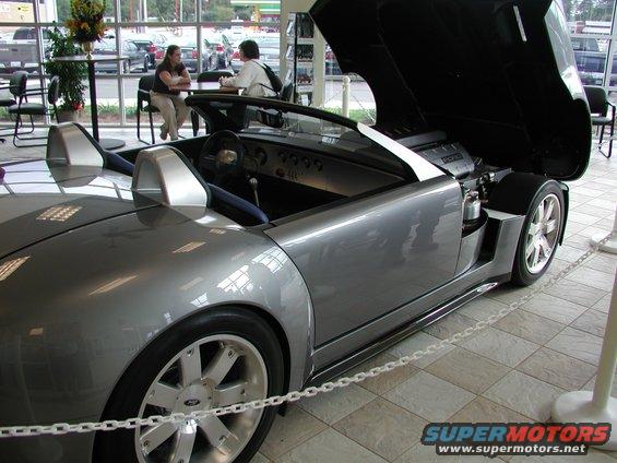 Silver Ford GT with hood open, showing engine and interior. Wheels have Ford logo