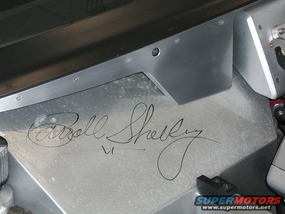 Carroll Shelby signature on a brushed aluminum panel, with "SUPERMOTORS.NET" visible at the bottom right