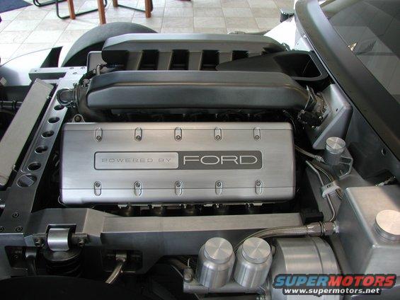 Engine bay with "Powered by Ford" inscribed on a silver cover, showing intake manifold and various metal components