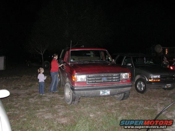 Red 1987 Ford Bronco parked next to a silver pickup truck at night