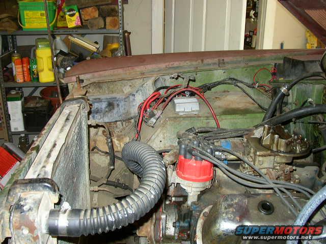 Engine bay with radiator, distributor, and carburetor visible. Rusty metal and wiring are prominent