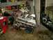 1995 Ford Bronco - An engine is hoisted by chains in a cluttered garage setting, with tools and shelves visible in the background.