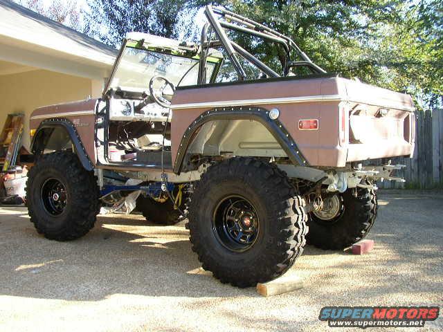 Brown 1978 Ford Bronco with large tires, roll cage, and removed doors
