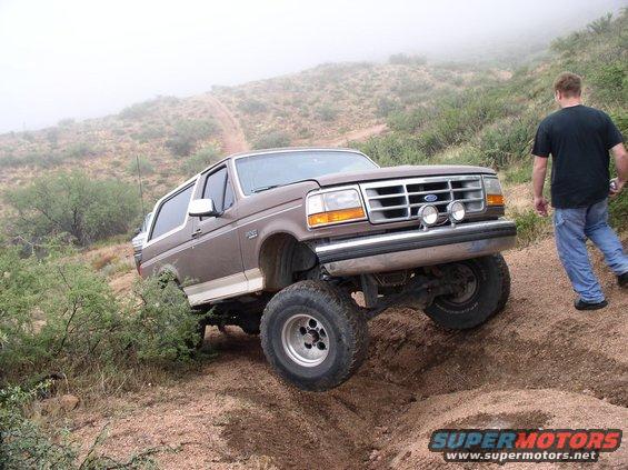 Brown 1990 Ford Bronco with lifted suspension driving off-road