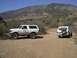 1988 Ford Bronco - Two white Ford Broncos are parked on a dirt road in a dry, mountainous landscape.