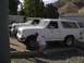 1988 Ford Bronco - A man inspects the tire of a white 1988 Ford Bronco, with another Ford truck visible behind it.