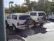 1988 Ford Bronco - Two white Ford Broncos and a white pickup truck are parked outdoors on a sunny day.