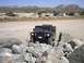 1988 Ford Bronco - A black Hummer H1 navigates a rocky terrain in a dry, open area with mountains in the background.