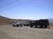 1988 Ford Bronco - Three off-road vehicles are parked on a dirt road with hills and mountains in the background.