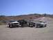 1988 Ford Bronco - A group of four-wheel drive vehicles are gathered in a dusty, outdoor setting with hills in the distance.
