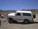 1988 Ford Bronco - Two white SUVs are parked in a dry, hilly landscape under a clear blue sky.