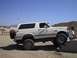1988 Ford Bronco - A white Ford Bronco is parked on a dirt surface with a person sitting on a concrete barrier nearby.