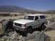 1988 Ford Bronco - White 1988 Ford Bronco driving over rocks in a desert landscape.
