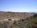 1988 Ford Bronco - A wide view of a dry, hilly terrain with scattered bushes and trees, and a clear sky above.