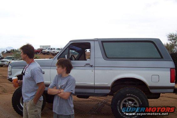 Two-tone gray and white 1992 Ford Bronco parked on dirt with two people standing nearby
