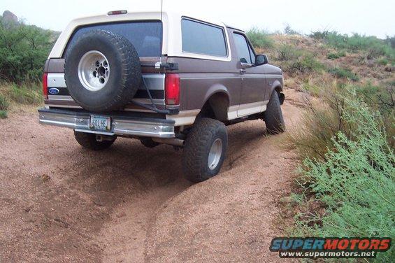 1992 Ford Bronco rear view with spare tire on back, driving on dirt road