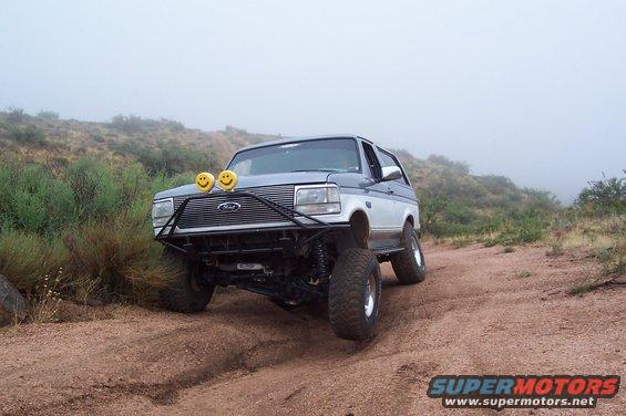 1992 Ford Bronco with custom bumper and smiley face lights on a dirt trail