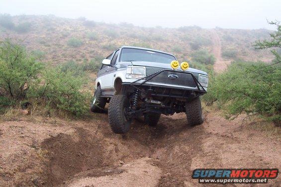 Ford Bronco climbing a dirt hill with a custom bumper and smiley face lights
