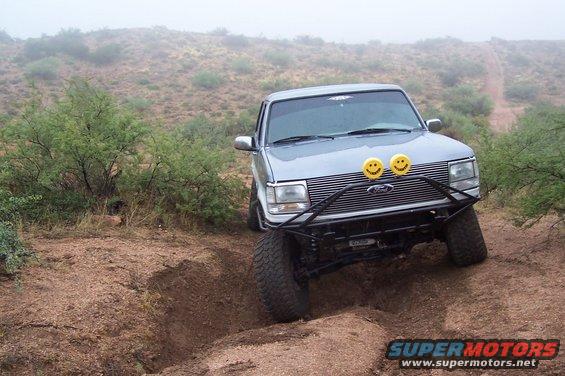 Silver SUV with custom bumper and smiley face lights on rough terrain