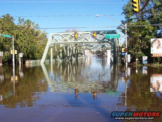 Flooded street with a bridge overhead. Traffic lights are visible above the water. A sign says Meadowbrook Ross Ave